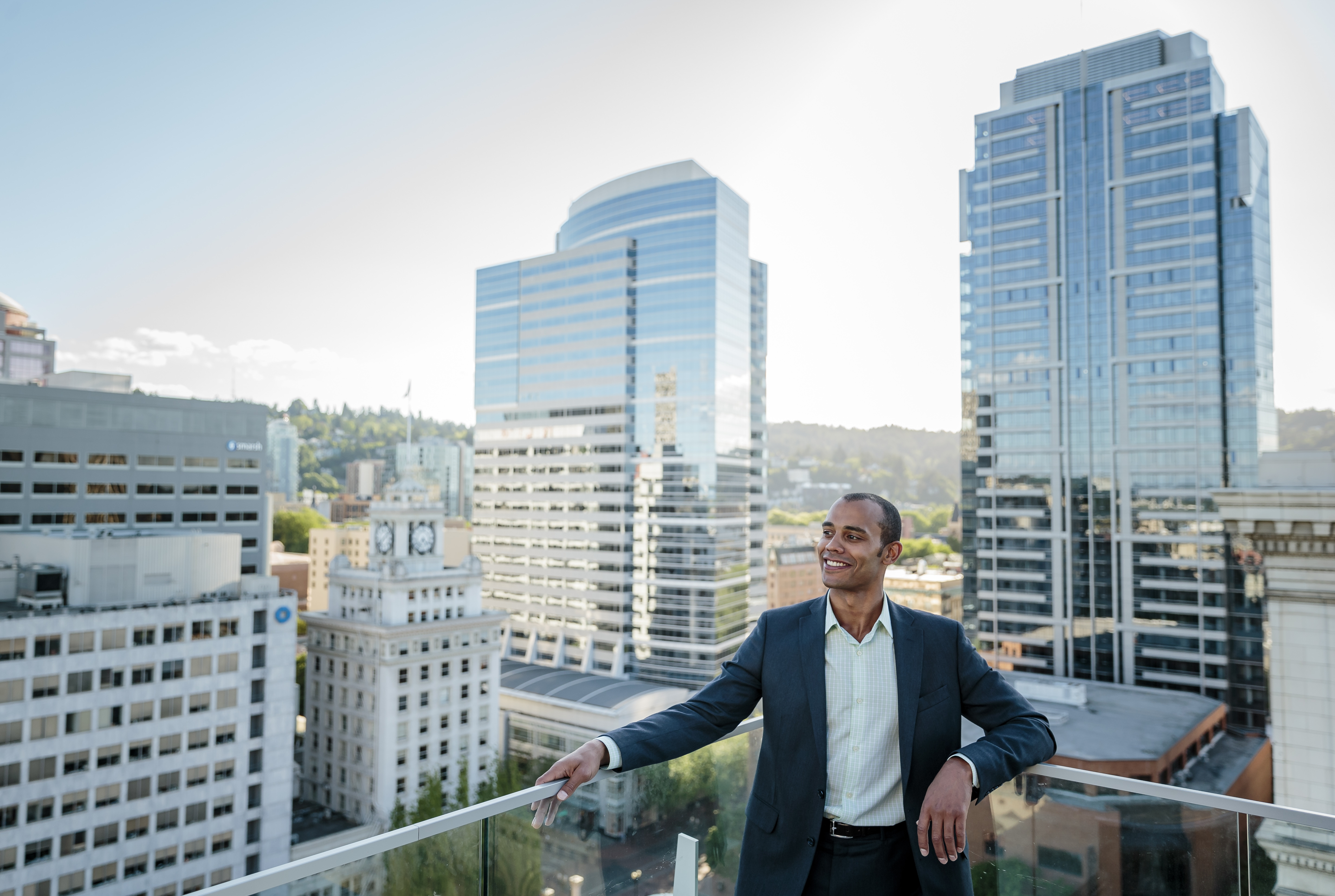 man in a suit standing on an outdoor patio with the Portland skyline in the background