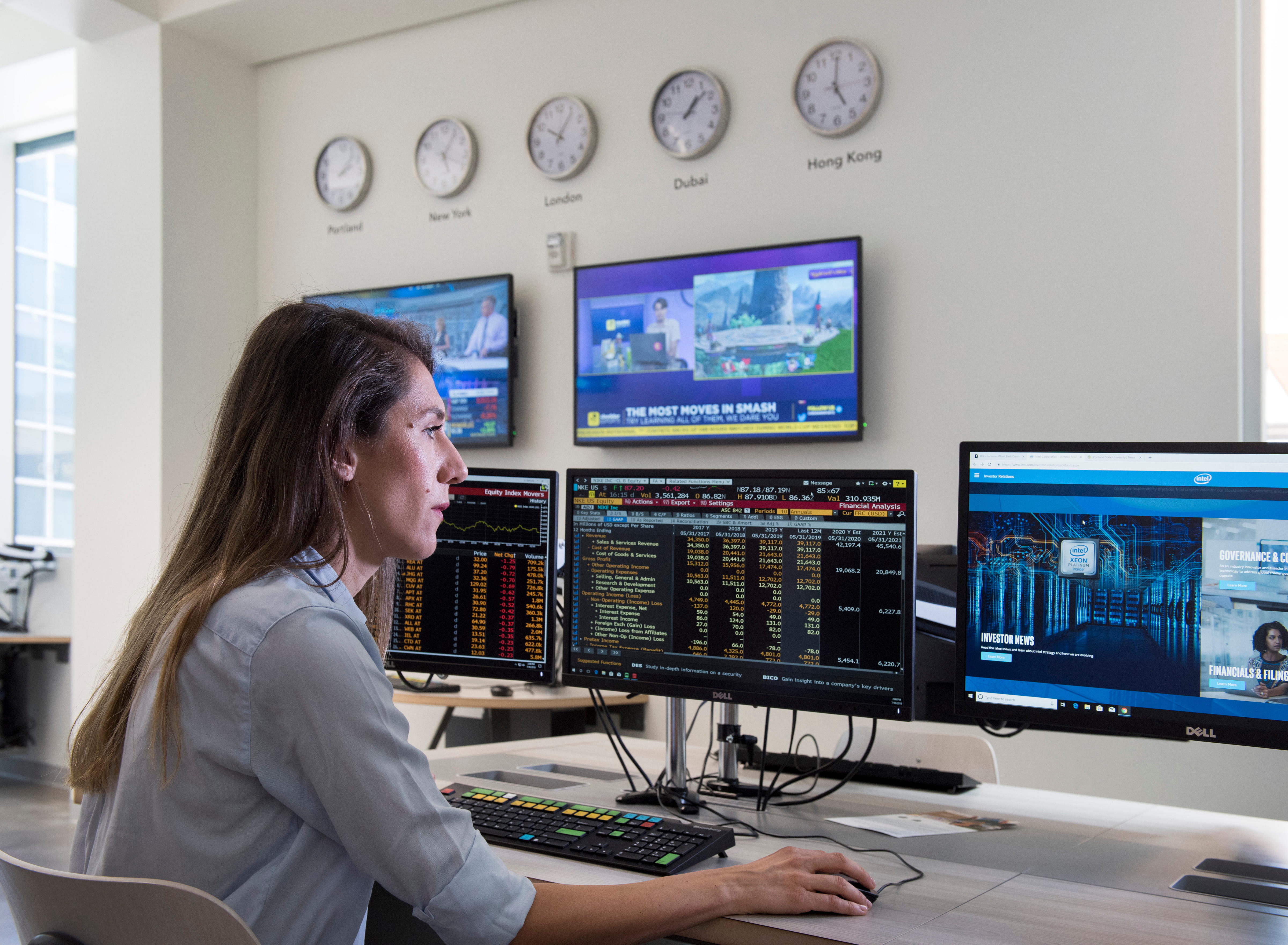 woman seated in front of a three computer monitors showing a variety of statistics