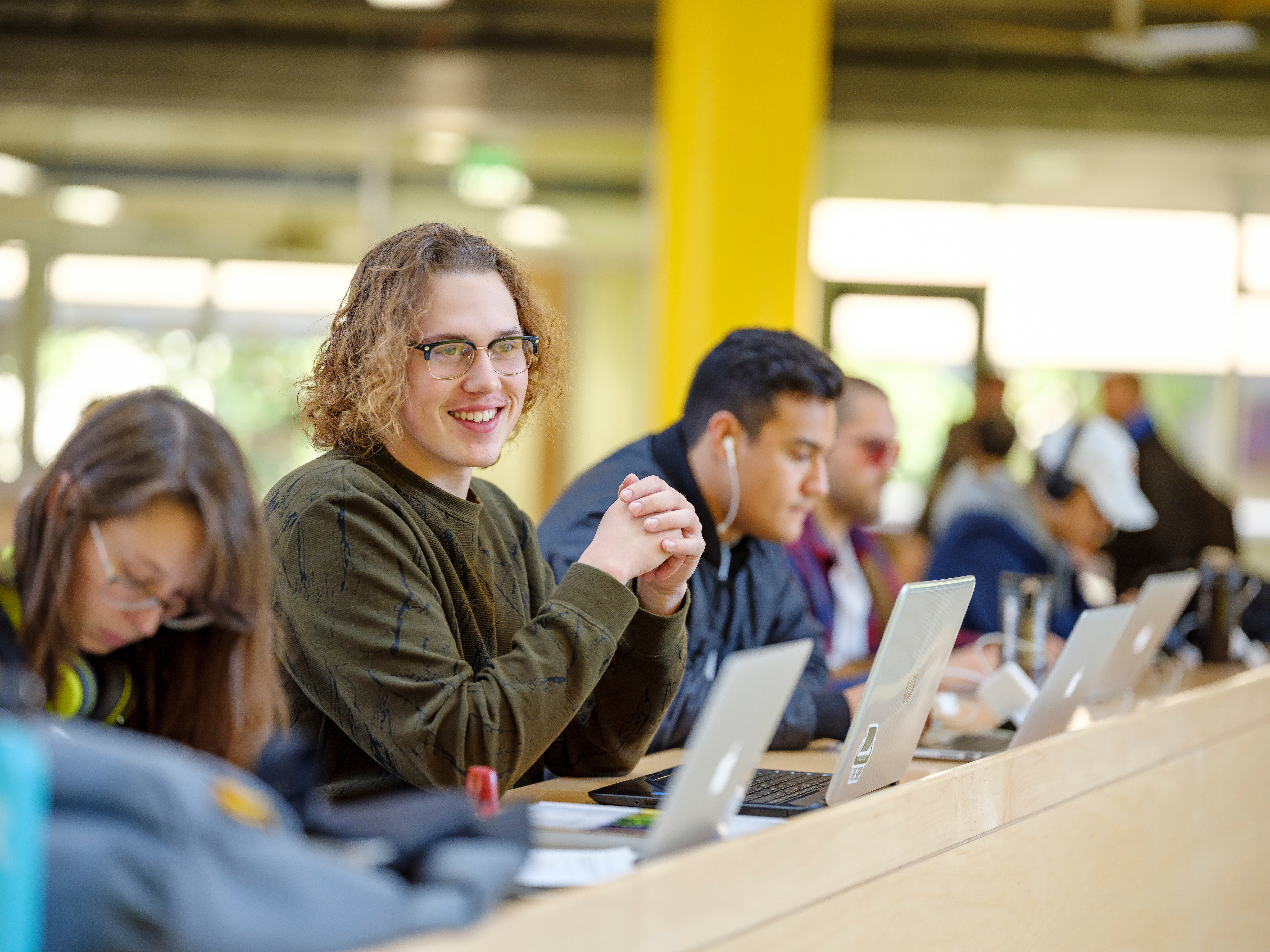 several students are seated at a long table, with laptops open in front of them.