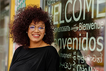 Student standing in front of a window with "Welcome" written in multiple languages