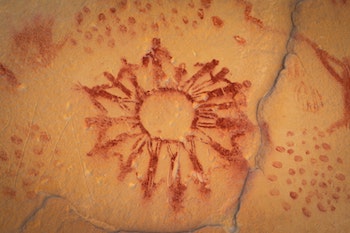 red petroglyph drawn on an ochre wall. the image depicts a group of people of various heights standing in a circle hoding hands