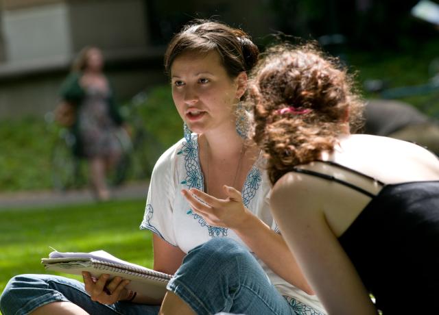 two students engaged in discussion, seated in the grass  in the PSU Park blocks