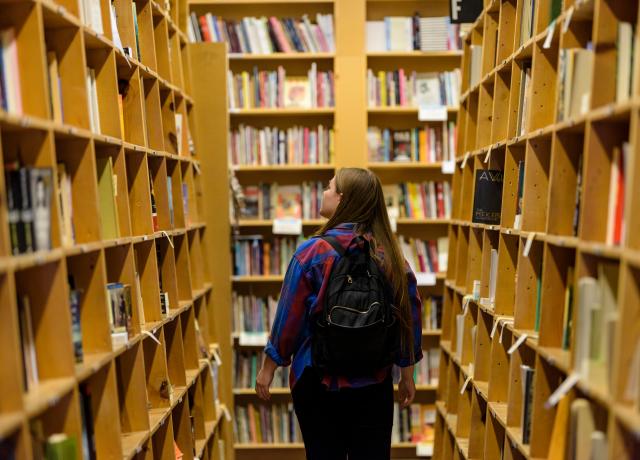 student wearing a backpack is walking through library bookshelves