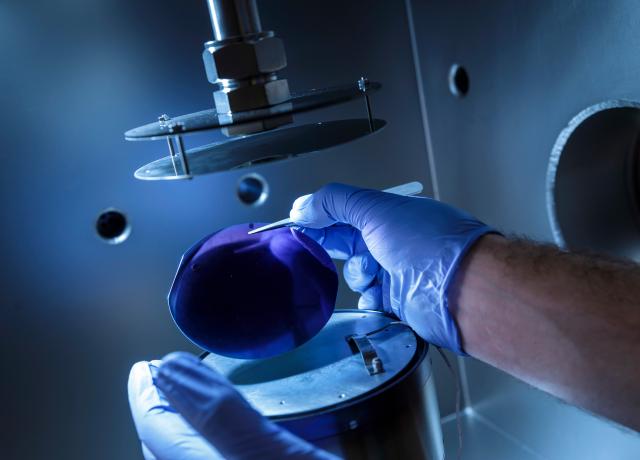 close up of two hands wearing lab gloves use tweezers to place a polished lens on an instrument