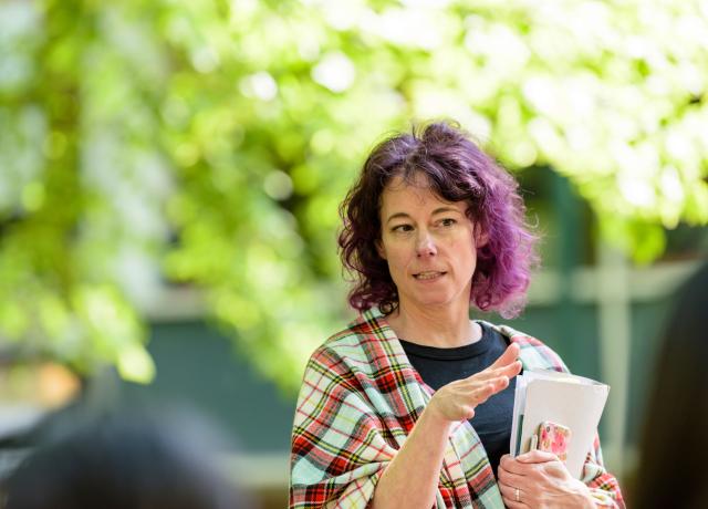 A person holding a manilla folder stands outside. they are gesturing with their hands while talking to somebody