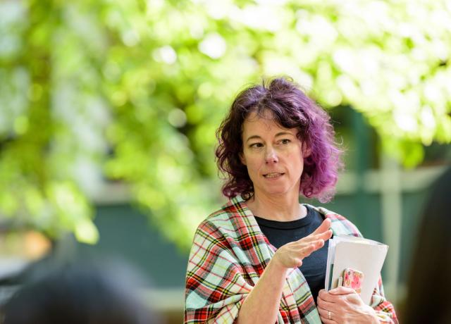 A person holding a manilla folder stands outside. they are gesturing with their hands while talking to somebody