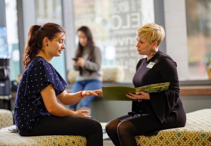 a student sits on benches with a PSU representative looking at a large brochure together