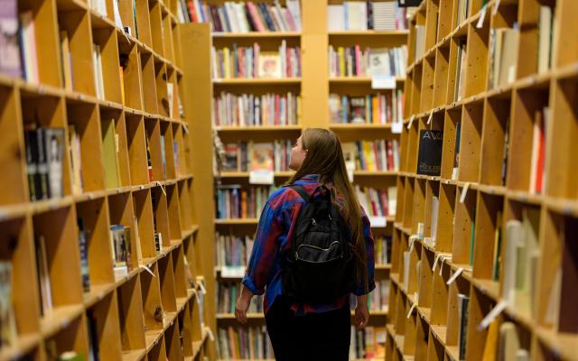 student wearing a backpack is walking through library bookshelves