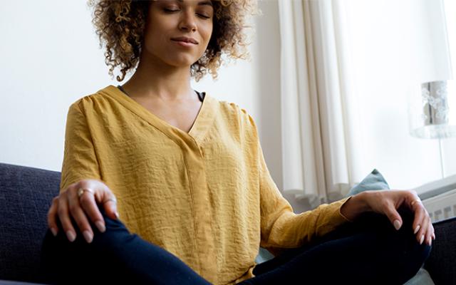 a person sits cross-legged with their hands resting on their knees. their eyes are closed in meditation
