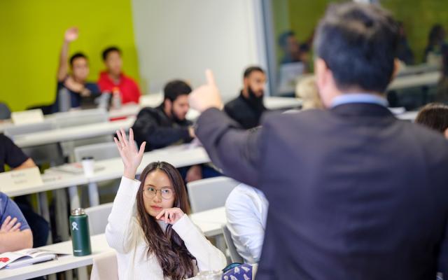 students in a classroom, a few students have their hand raised