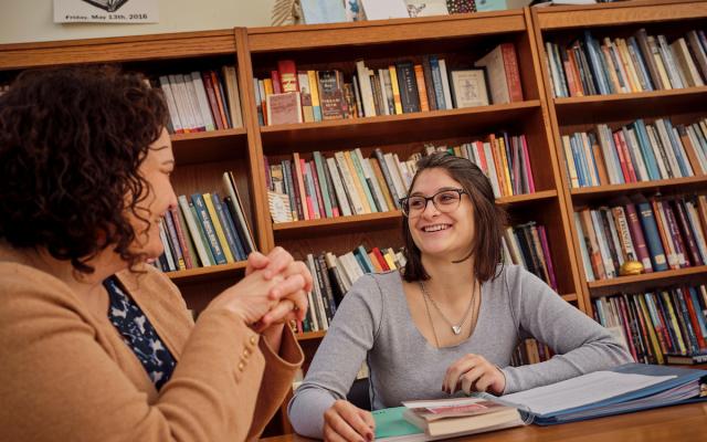 Image of two individuals in library sitting and smiling.