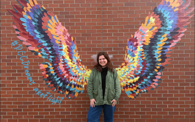 person standing in front of a mural of colorful wings