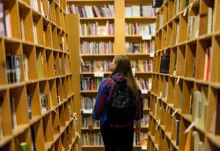student wearing a backpack is walking through library bookshelves