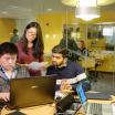 Three students around a table looking at a laptop. One student appears to be typing