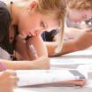 students leaned over a table in concentration writing on paper and worksheets