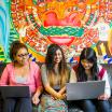 three students sitting in front of a colorful mural
