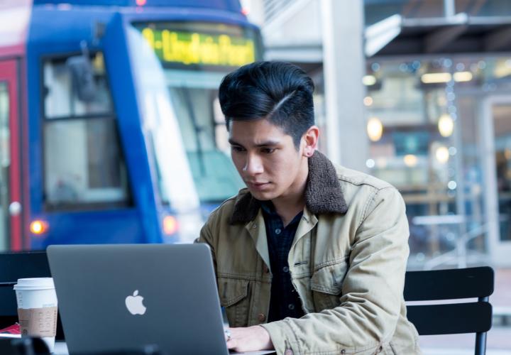Student works on a laptop outdoors with a Portland Streetcar in the background