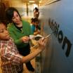 Faculty member and a grade school student paint the word nutrition on hallway wall