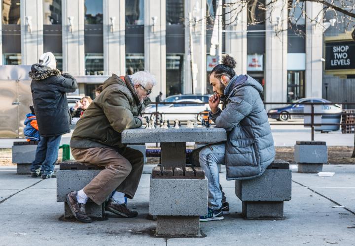 Young man and elderly man playing chess in the park