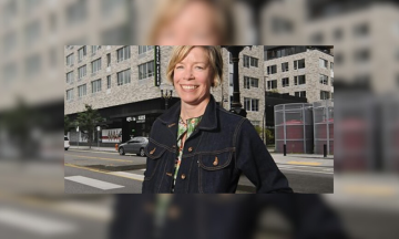 Sarah Heinicke stands in a dark denim jacket in front of a city block.