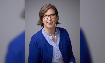 Moriah McSharry McGrath smiles at the camera. She has light brown hair and is wearing a royal blue cardigan over a blue and white striped collared shirt.