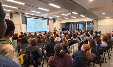 An audience watches a presentation on heat resilience focus areas delivered by MURP student Luke Gordon in a crowded lecture hall at the 2026 MURP Workshop Kickoff. 
