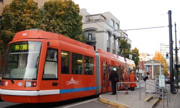An orange streetcar in Portland stops to pick up passengers.