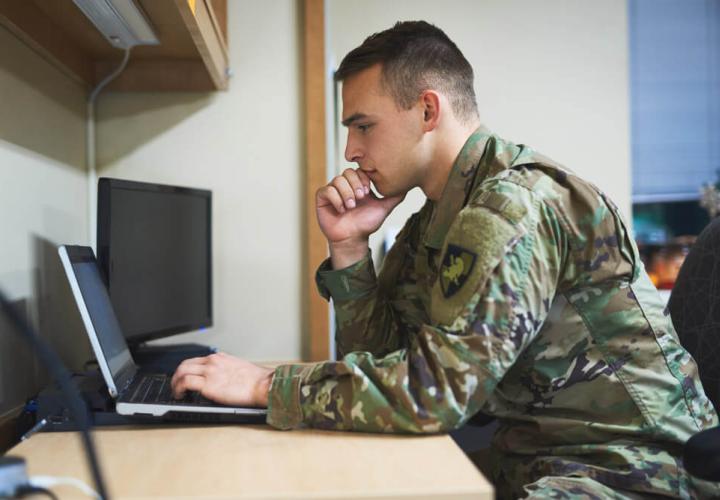 a man in a green army uniform gazes pensively at a turned off computer
