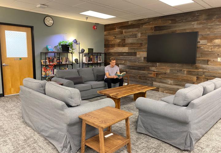 a man reads a book on a couch alone, surrounded by other lonely couches.