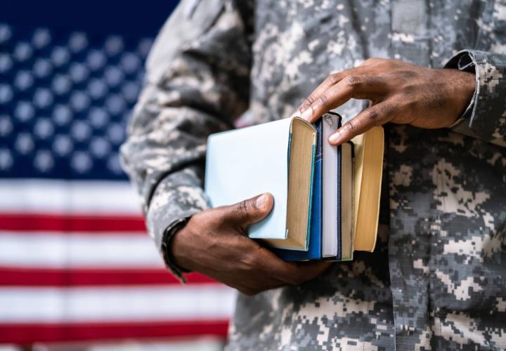 a man in blue camo holds some books in front of the us flag