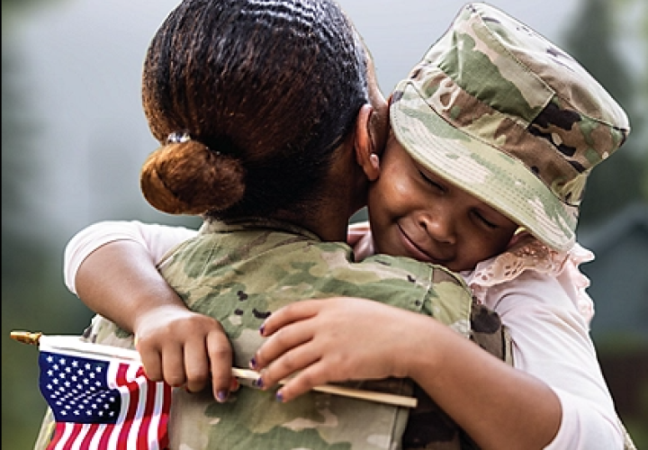 Young child wearing a military Patrol Cap hugging woman wearing a military uniform