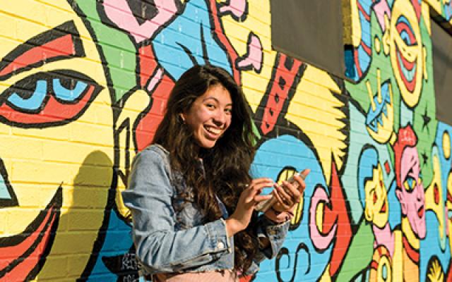 Student on her phone in front of a mural
