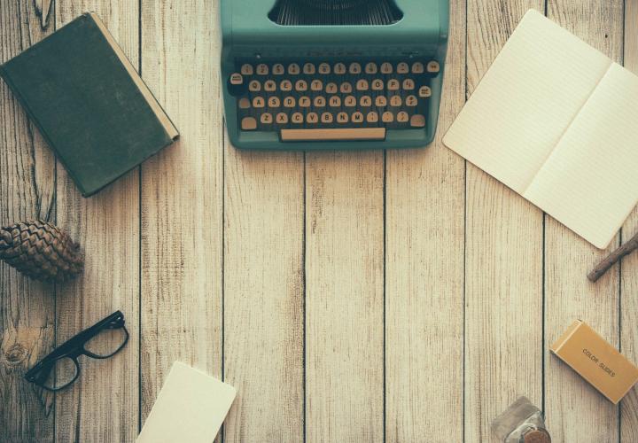a typewriter, book, and notebook on an old wooden desk